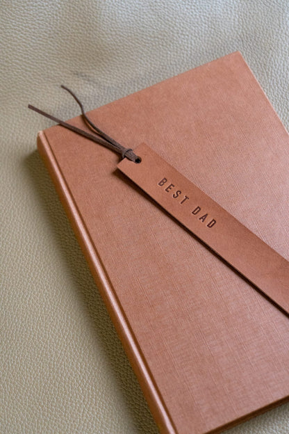 a beige leather bookmark engraved "BEST DAD" sits on a closed book 