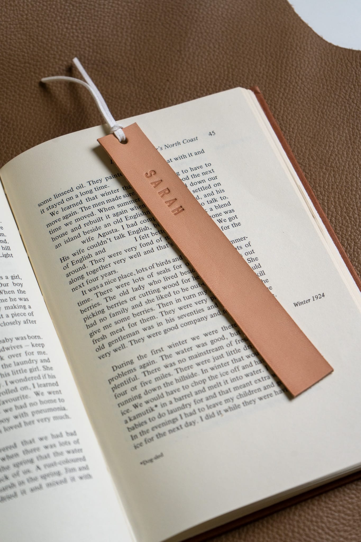 a beige leather bookmark engraved "SARAH" sits on an open book 