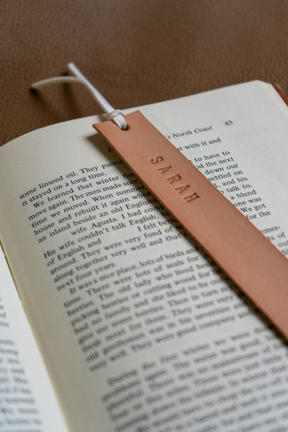 a beige leather bookmark engraved "SARAH" sits on an open book 