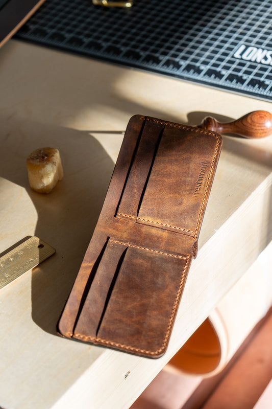 A brown bifold wallet made of leather, displayed on a wooden surface, showcasing its multiple card slots and a cash compartment.