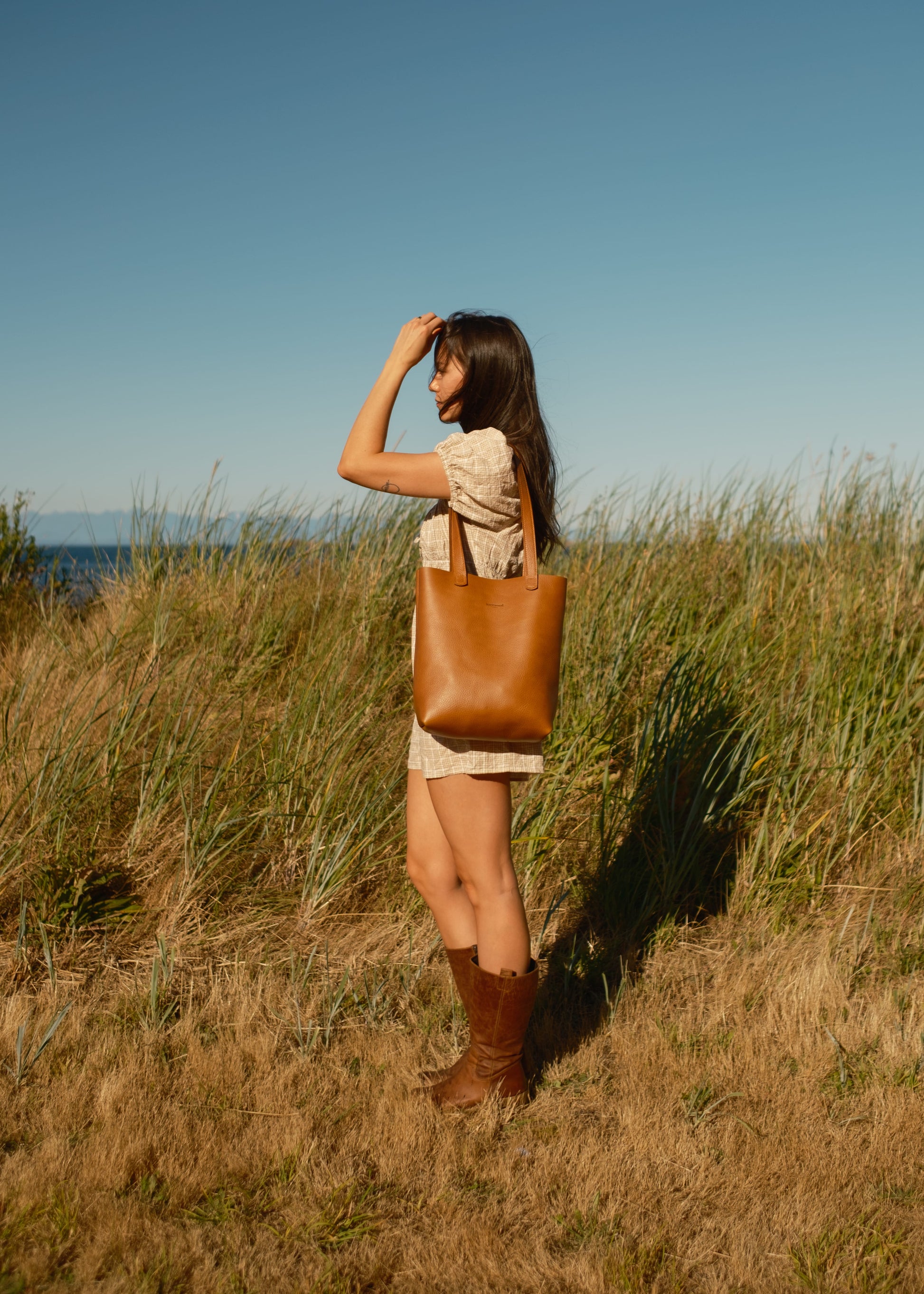 Woman standing in a field with a brown leather bag