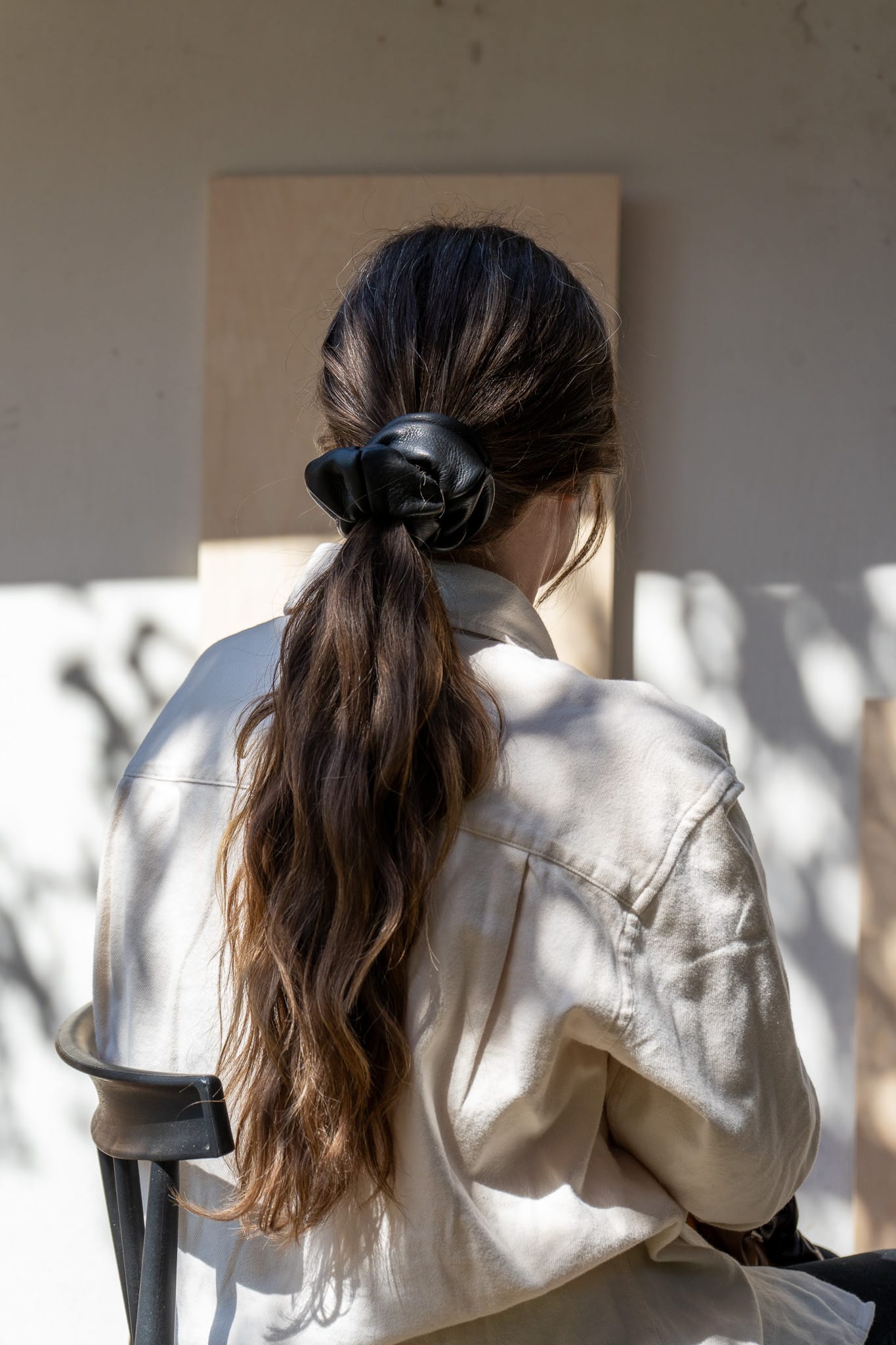 Person with long hair in a ponytail wearing a beige shirt, sitting outdoors.
