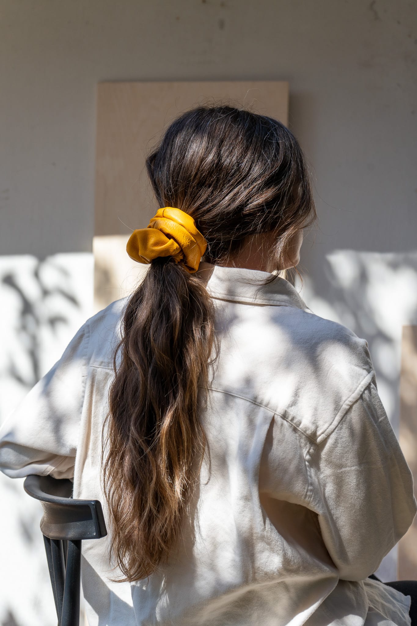 Person with long hair in a ponytail wearing a yellow scrunchie, sitting outdoors.