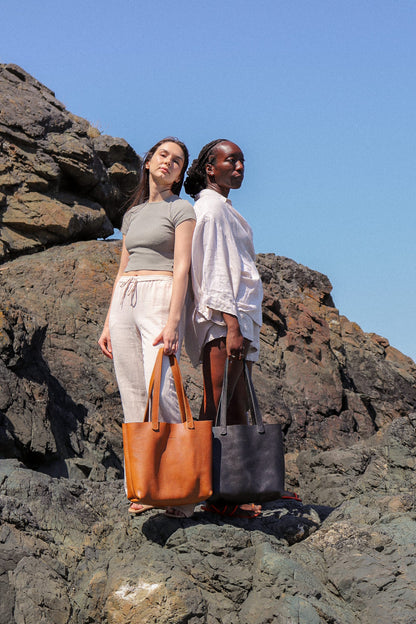 two women stand on a rocky hill holding a brown and black tote bag
