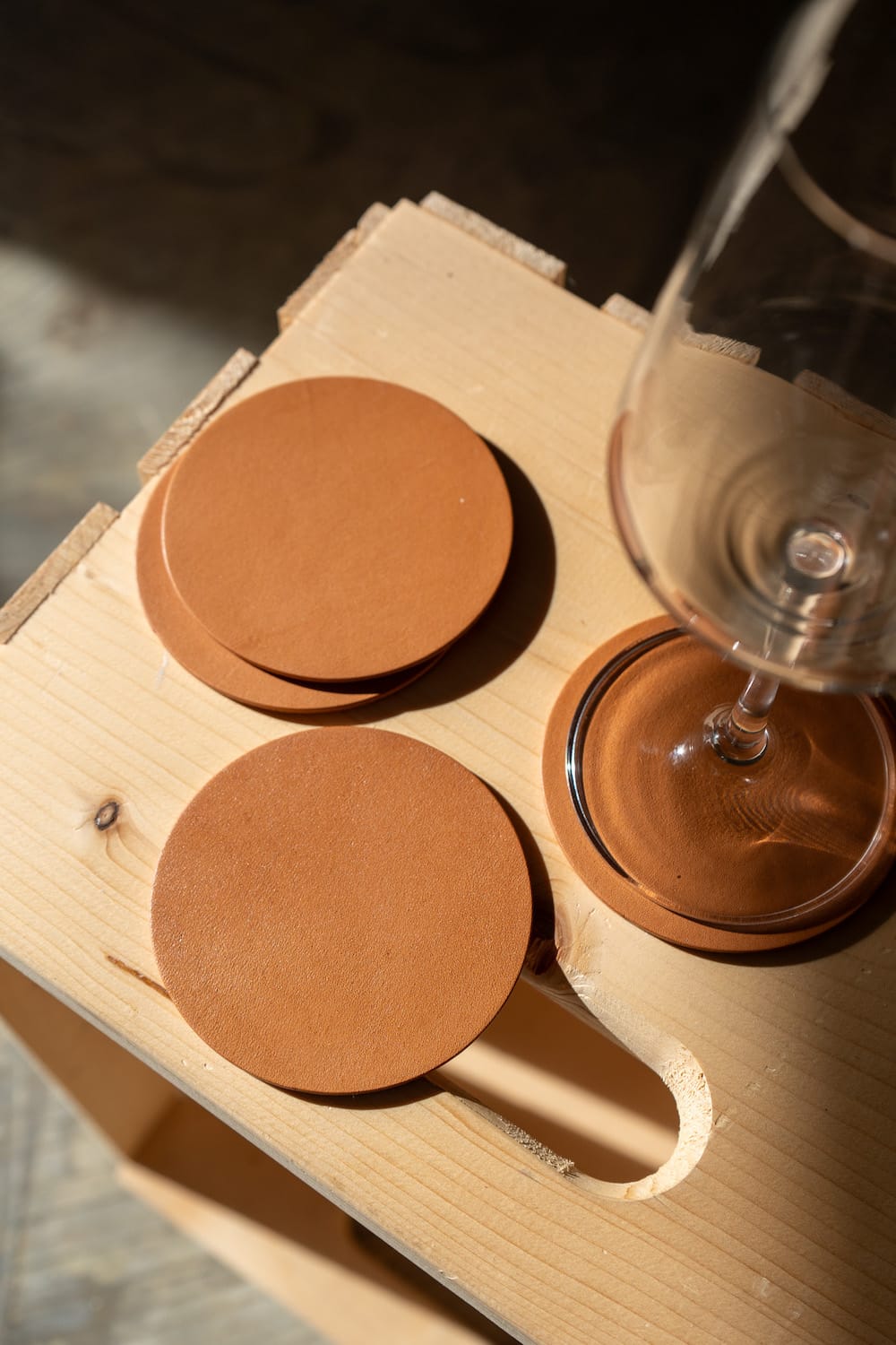 A set of round, brown leather coasters  displayed on a wooden surface with a glass in the background.