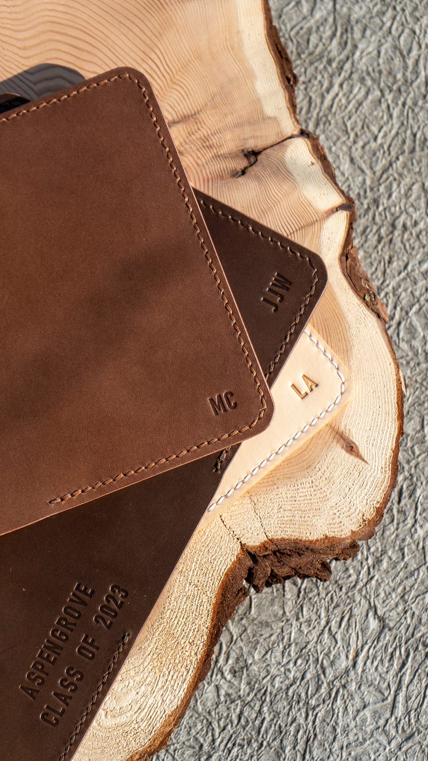leather passport covers in different neutral colours sit on a wooden background with initials stamped into them