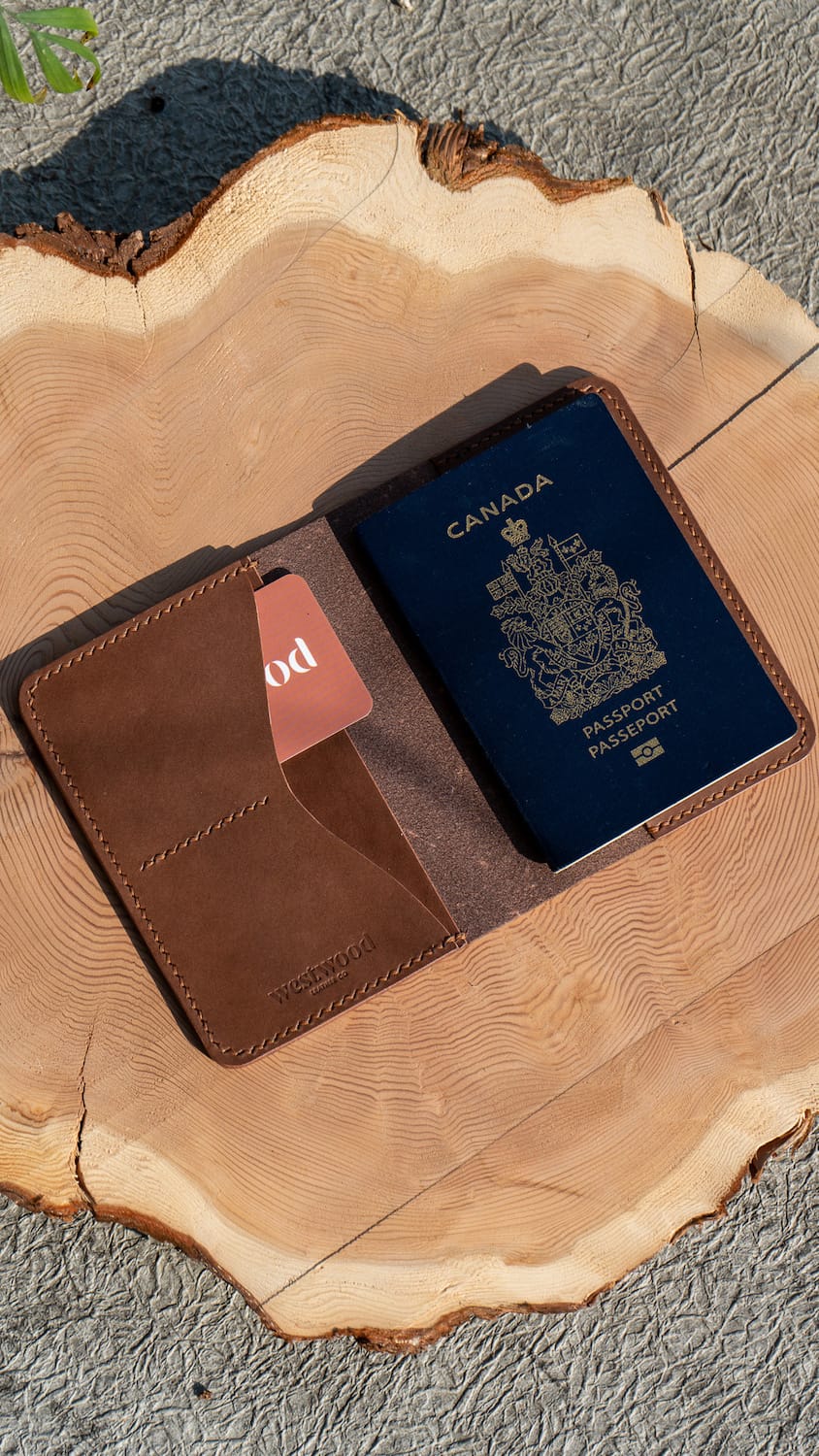 A brown leather passport wallet opened to display the interior card slots and the slot to slide a passport into. A passport is visible inside the wallet.