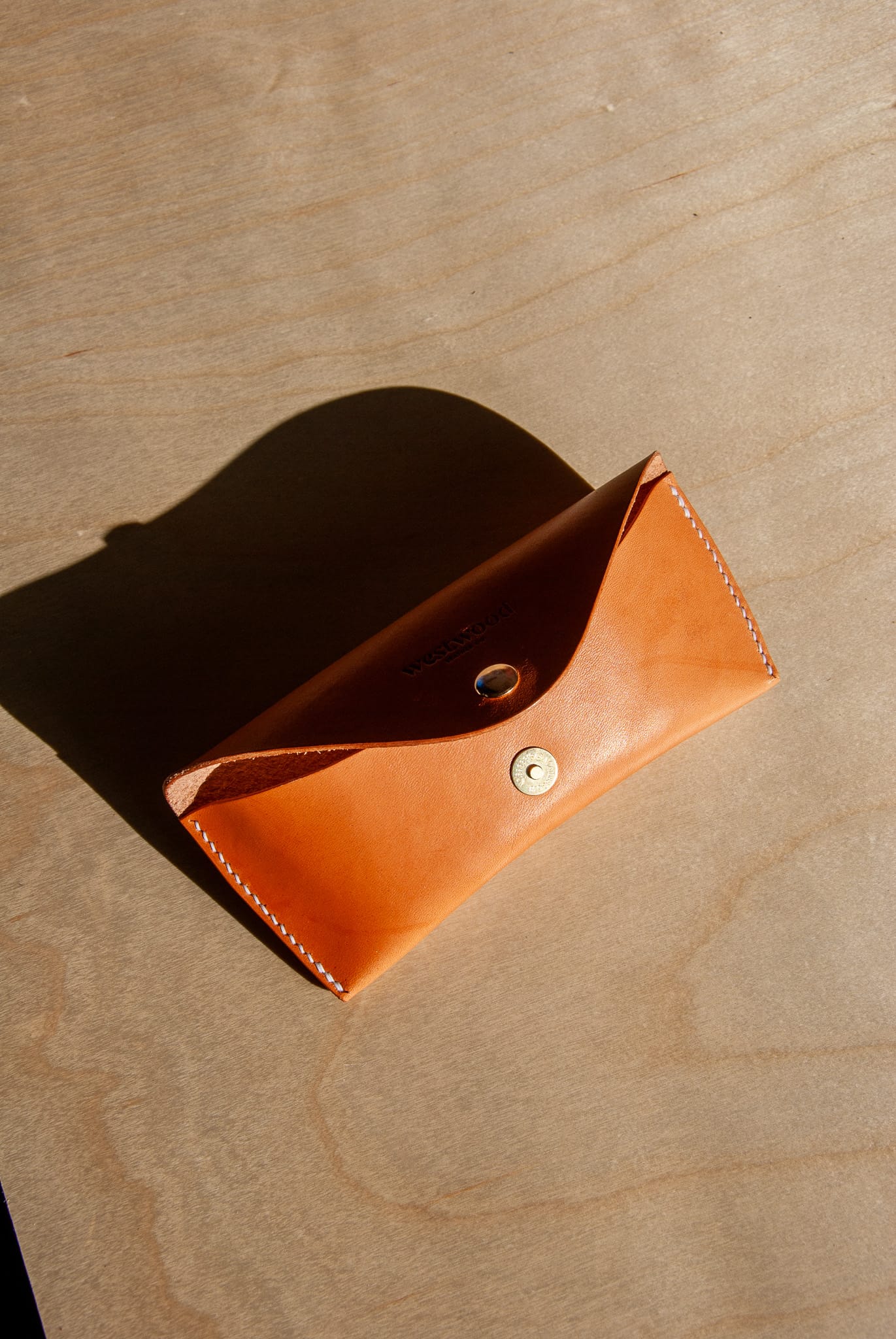 Brown leather pouch with a button on a beige surface