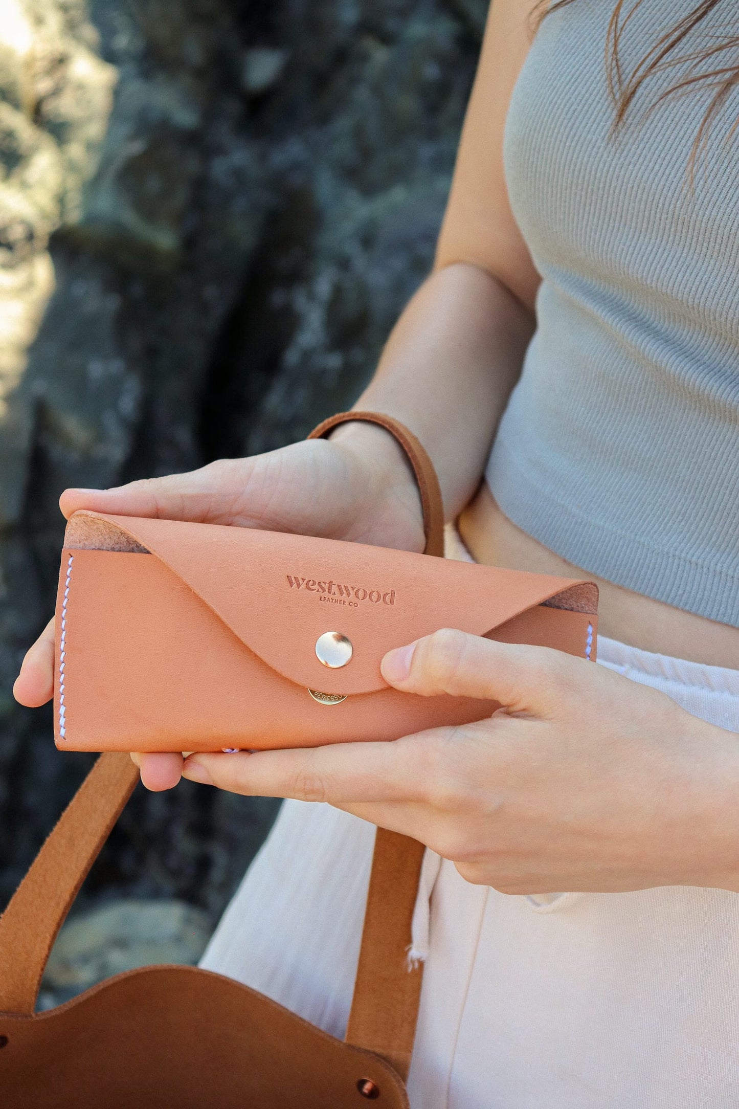 Person holding a tan glasses case with 'Westwood' branding against a blurred natural background