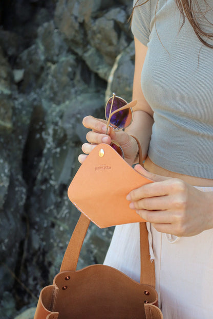 Person holding a peach-colored pouch with sunglasses, standing against a rocky background
