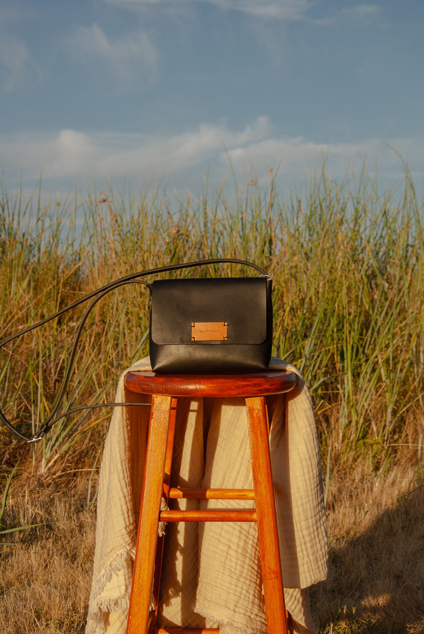 Black leather bag on a wooden stool in a grassy field with a blue sky.