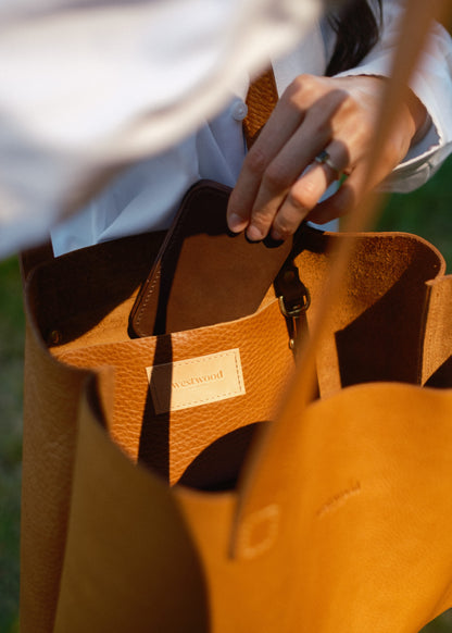 Brown leather bag with visible brand name held by a person in a white shirt.