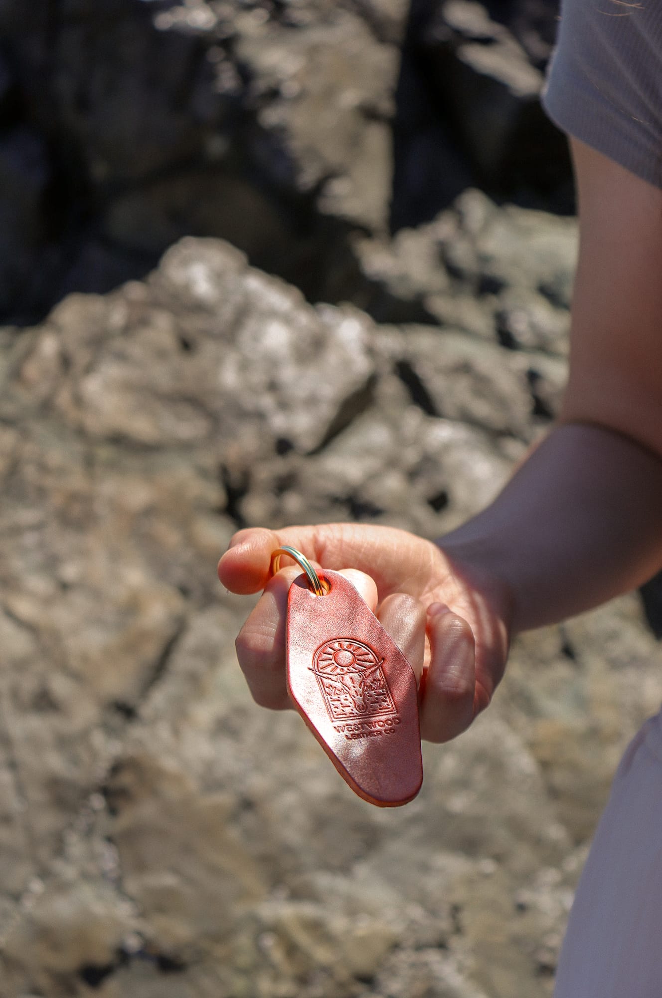 a person holds a brown leather keychain with a brass key ring, in front of a rock