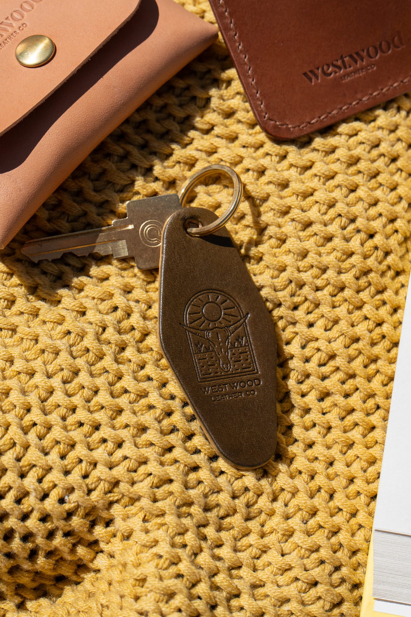 A green leather keychain with a brass key ring, on a yellow blanket.