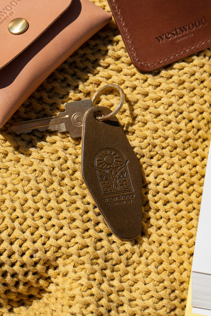 A green leather keychain with a brass key ring, on a yellow blanket.