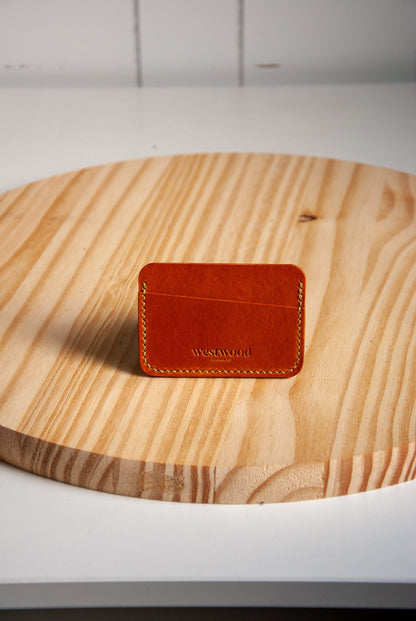 Brown leather cardholder with 'WESTWOOD' branding on a wooden surface
