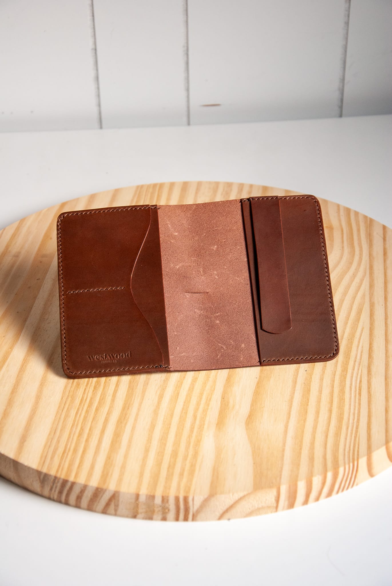Brown leather wallet on a wooden surface with a white cushioned background