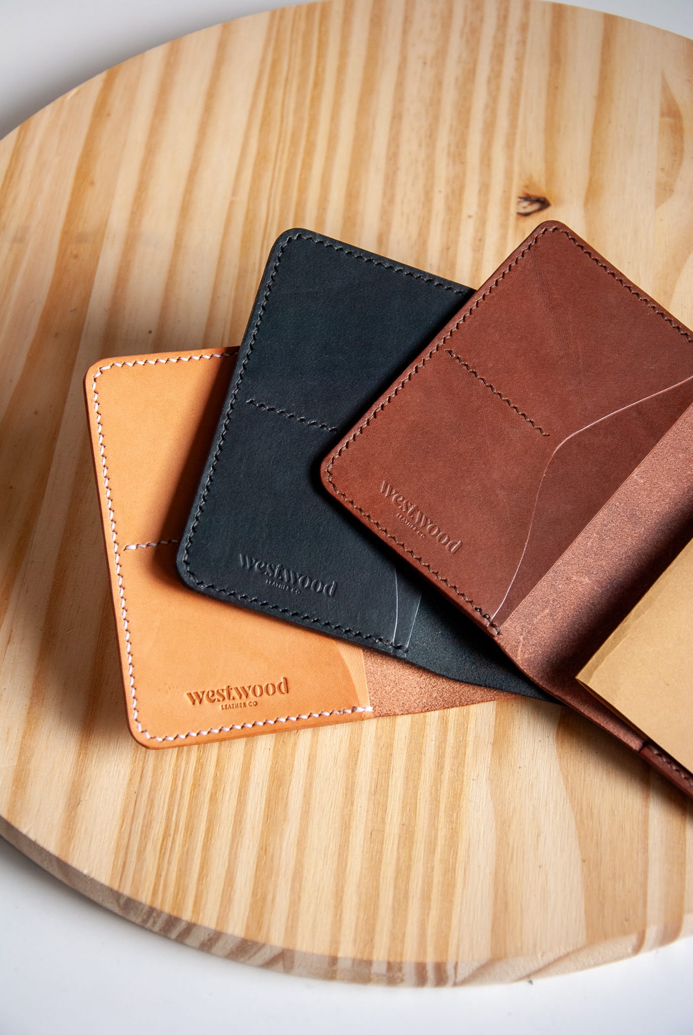 Three leather card holders in brown, black, and orange on a wooden surface with 'Westwood' branding.