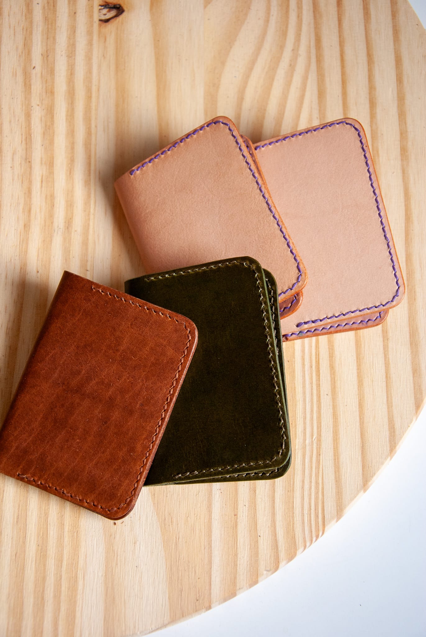 Four leather wallets in brown, black, and beige on a wooden surface.