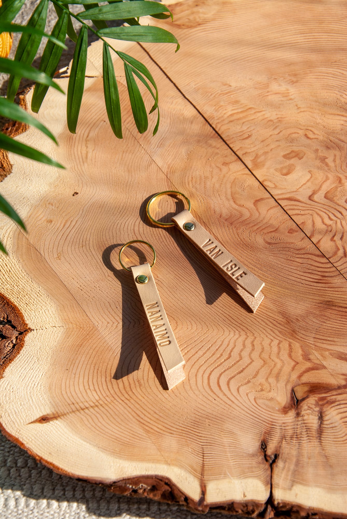 two beige leather keychains with gold key rings with engraving on a wooden surface